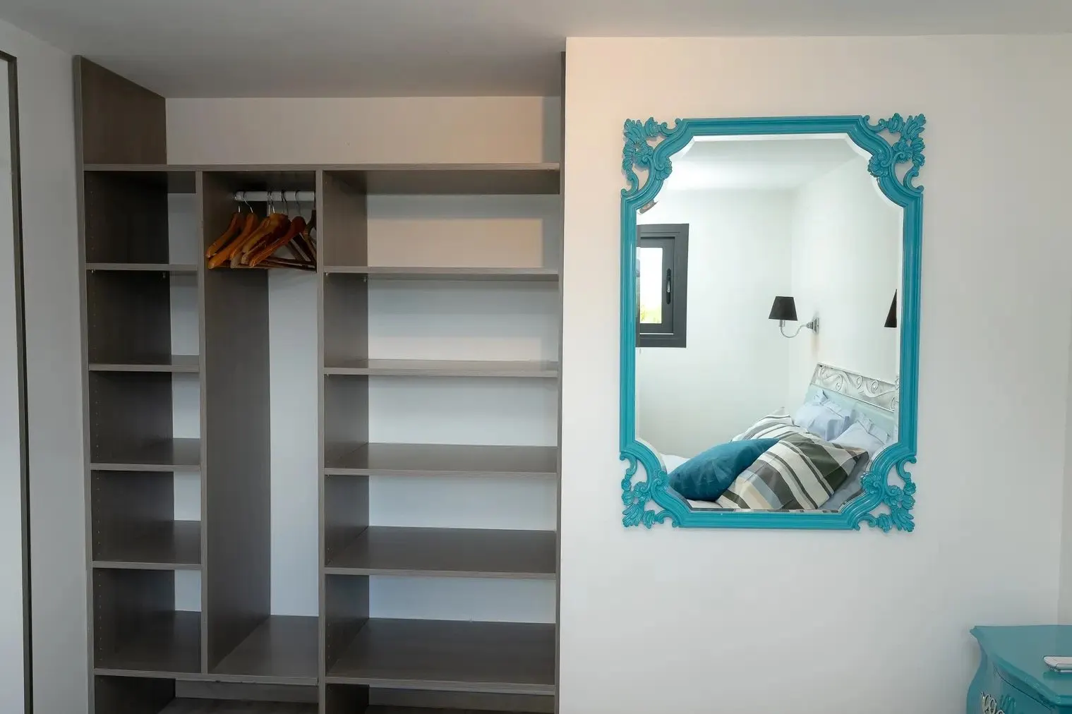 An open wardrobe and a turquoise baroque mirror in the bedroom