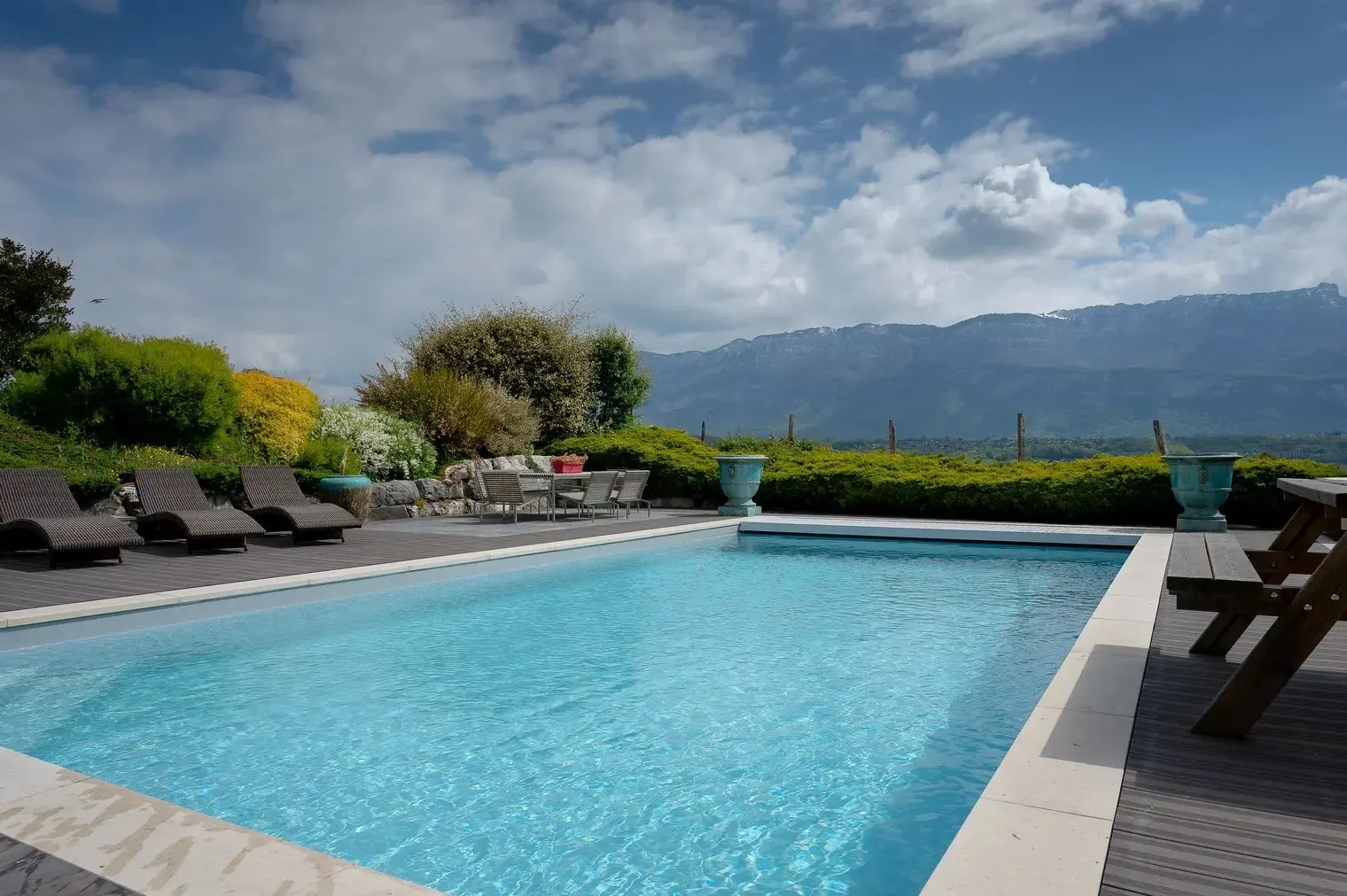 The pool under white clouds, with loungers lined up along the hedge